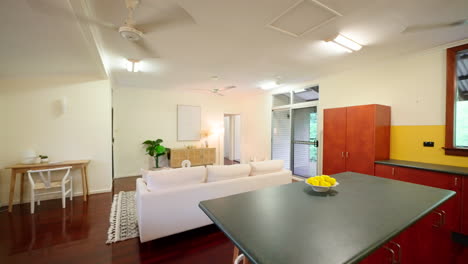 pullback from colourful yellow wall house with wooden floorboard cabinets around lounge dining kitchen open plan living area, corrugated roof