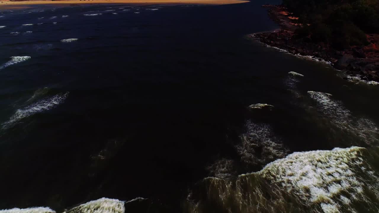 imágenes de drones siguiendo las olas rompiendo en una playa rocosa, filmadas en el sur de goa