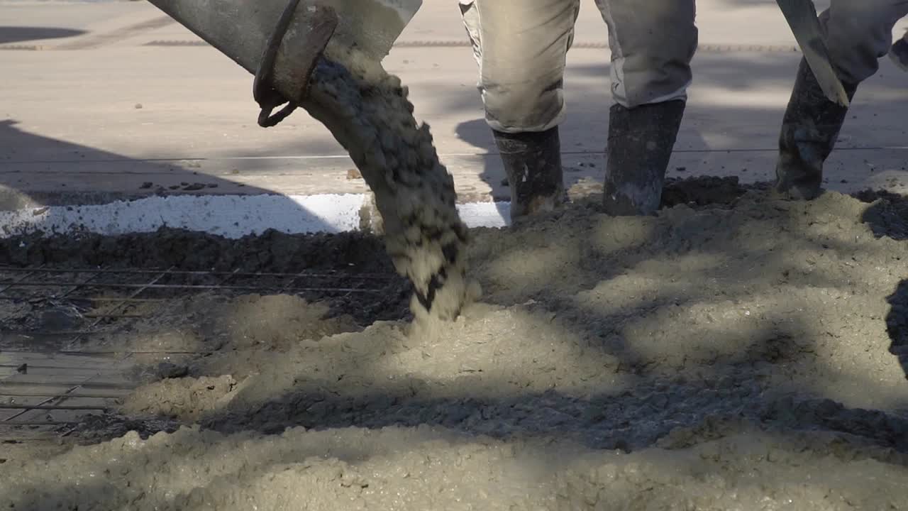 A mixer truck lays fresh asphalt onto a street while workers use shovels to spread it evenly.