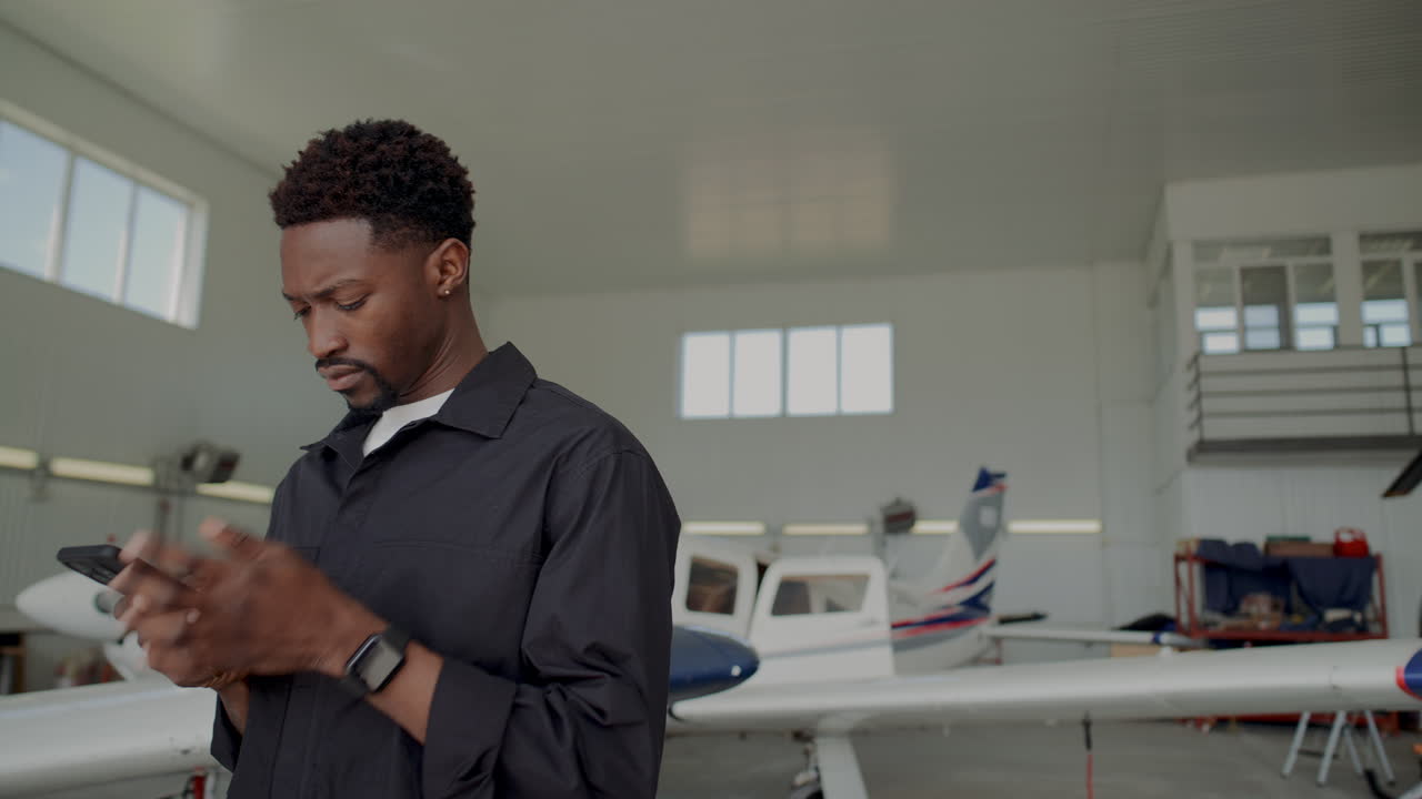 Black Aviation Mechanic Browsing the Web on His Phone in Hangar