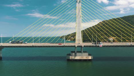 drone aerial side panning view of concrete cable-stayed bridge traffic above turquoise color ocean