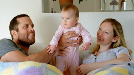 front view of mid adult caucasian parents playing and holding baby on bed in a comfortable home 4k