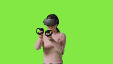 mujer con auriculares de realidad virtual y jugando contra el fondo de un estudio de pantalla verde