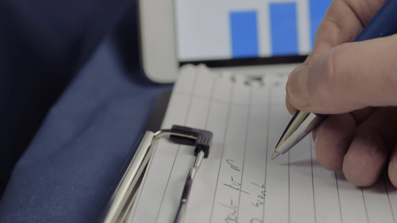 Writing sales report on clipboard with blue graph in background close up