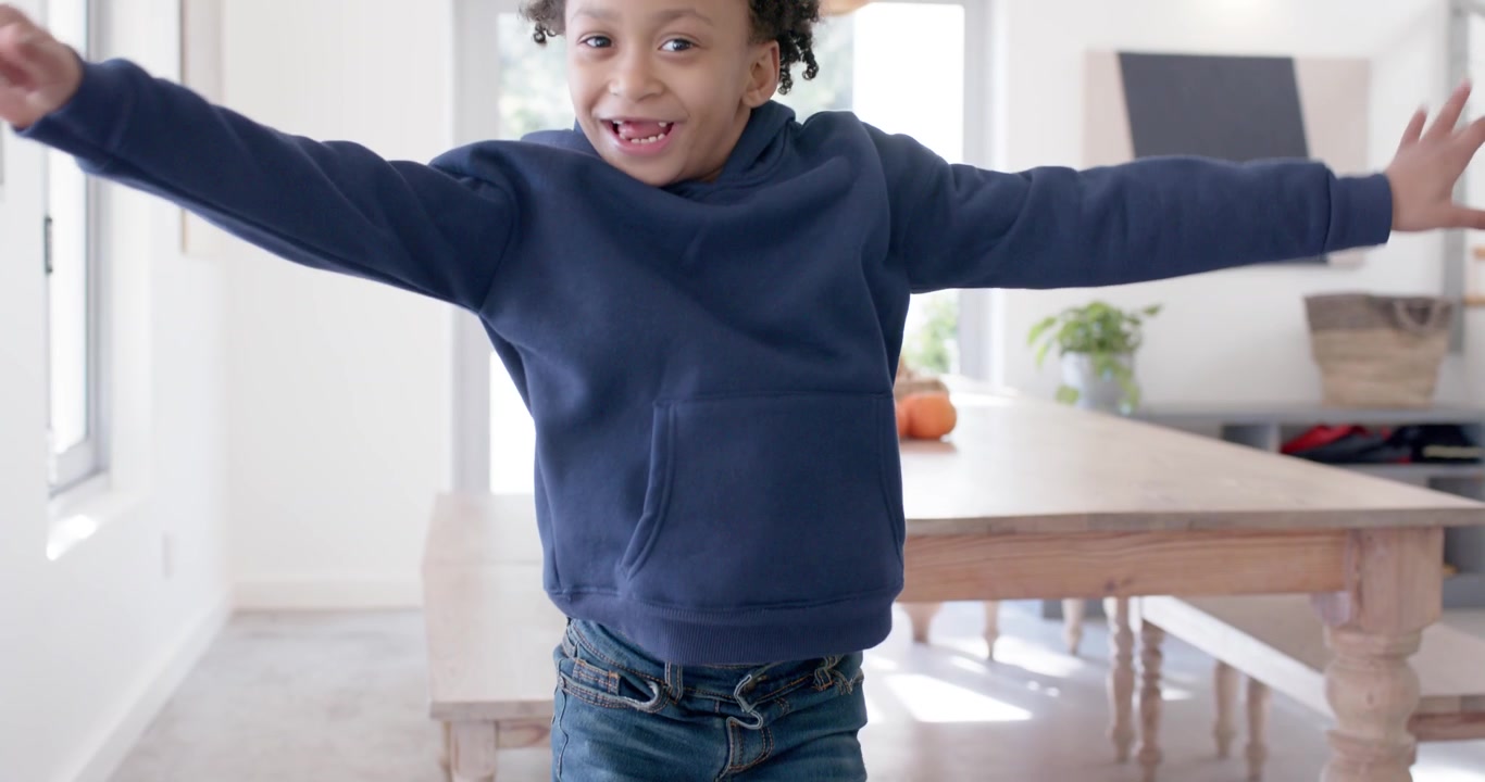 African American child in hoodie entering dining area running to cam smiling showing missing tooth