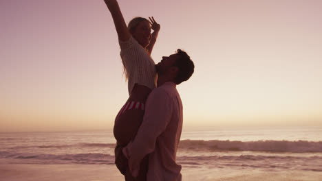 una pareja caucásica disfrutando del tiempo en la playa durante la puesta de sol