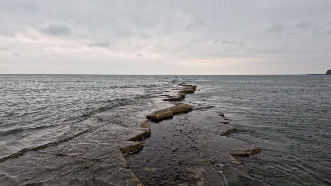 Kimmeridge bay, Dorest, walking over water level rocks out of the bay. Gentle waves over the underwater rock ledge. Water splashing over the rocks and the stabilised camera walks along them.
