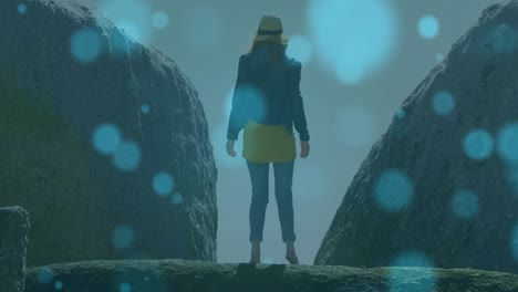 Animation-of-glowing-spots-over-caucasian-woman-standing-on-rock