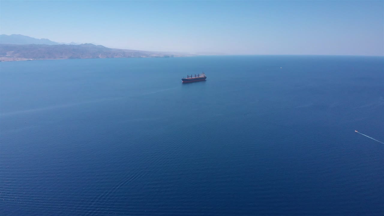 Aerial view of a large cargo ship sailing on a vast blue ocean with distant land