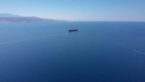aerial view of a large cargo ship sailing on a vast blue ocean with distant land