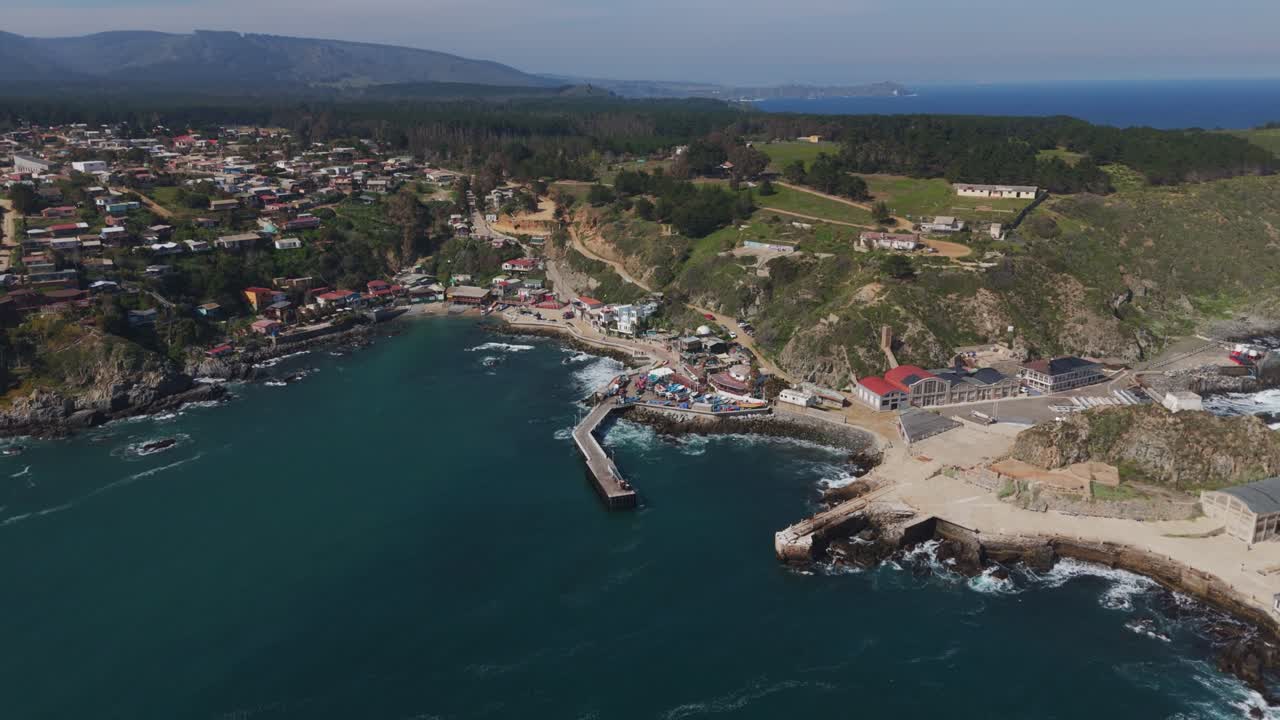 Aerial view of Caleta Quintay harbour with a vast coastline in Chile. The picturesque landscape features a marina with surrounding natural beauty and coastal buildings.