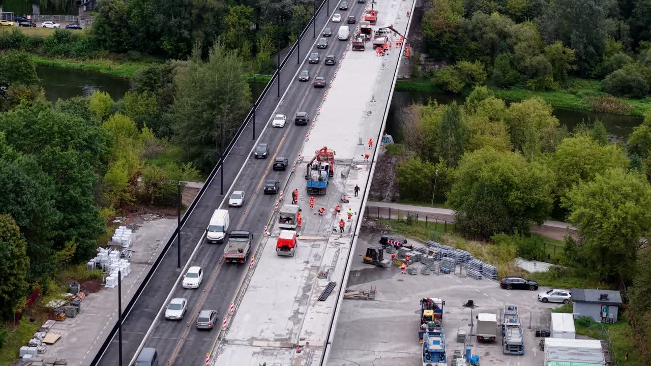 Drone-luchtfoto toont de reparatie van een snelwegbrug met een afgesloten rijstrook en gestaag verkeer naast een groen parkgebied, waarbij de werkzaamheden aan de weg en de pendelvoertuigen overdag worden vastgelegd