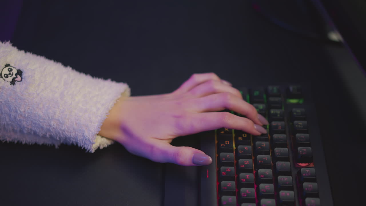 Top down view of girl hand in fluffy sweater with teddy bear print typing on illuminated mechanical keyboard, surrounded by ambient light glow from gaming setup