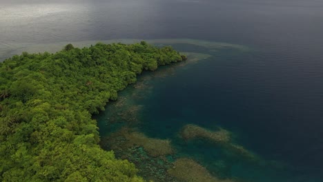 Aerial-shot-moving-backwards-showing-a-seascape-view-of-a-very-green-and-lush-little-island-with-cliffs,-rocks-and-a-beach