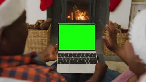 Pareja-Afroamericana-Saludando-Con-Sombreros-De-Papá-Noel-Haciendo-Videollamadas-Navideñas-Con-Laptop,-Con-Pantalla-Verde