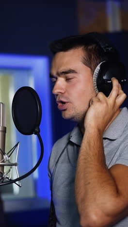male singer performing his song emotionally in studio. man sings near the professional microphone holding his hand by the headphone. vertical video