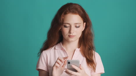 Redheaded girl in front of camera on turquoise background.