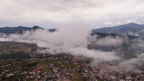 thick fluffy clouds hover over a village with red roofs, nestled near the mountains.