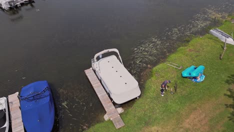 hombre cortando el césped con un cortador de césped en la orilla del río cerca del muelle de barcos