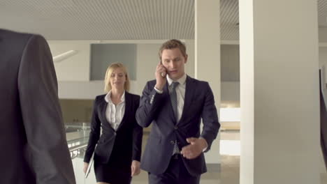 businessmen and businesswoman walking around the office, one of them talking on the phone accompanied by a blonde woman