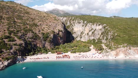 Luftdrohnenansicht-Von-Gjipe-Beach-Und-Canyon,-Dhermi,-Albanien---Versteckte-Paraside-Mit-Booten,-Touristen,-Sonnenliegen-Und-Blauem-Meer