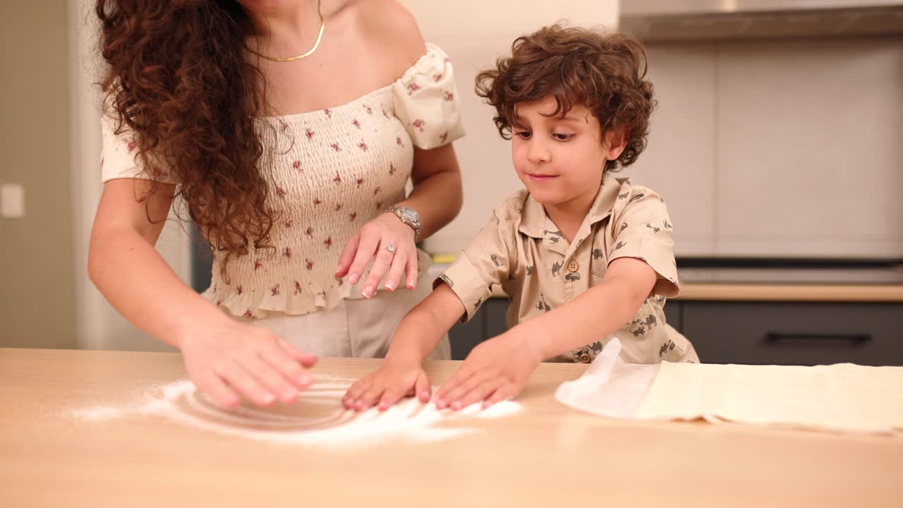 Mother and son spreading flour on kitchen table