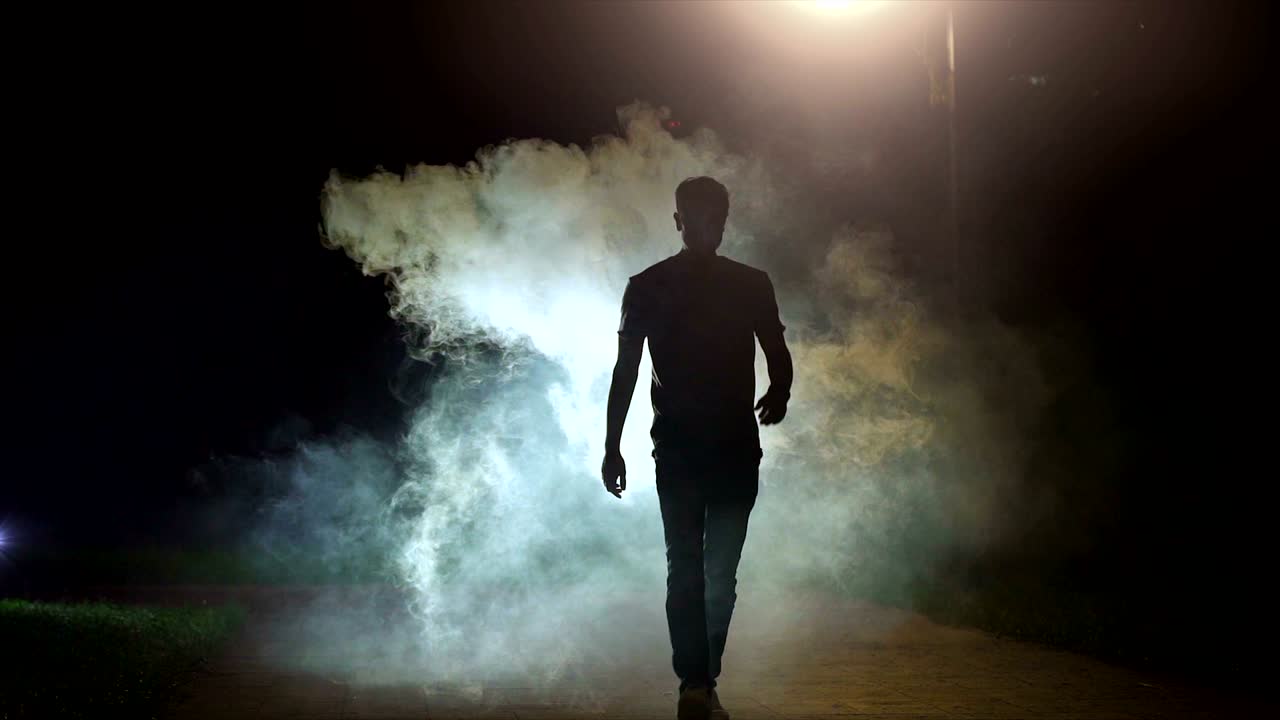 The man walking near the cloud of smoke on the dark background, slow motion