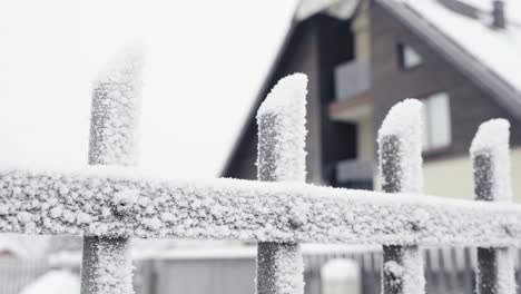 frozen fence covered with snow and ice, cold winter day, blurred house behind