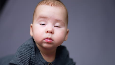 healthy caucasian toddler boy looks up lifting little eyebrows and smiling. portrait of an adorable kid in grey shirt. close up. blurred backdrop.