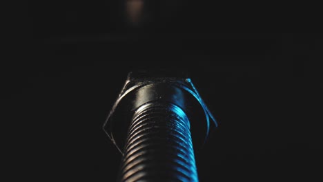 macro slow push out shot of the thread of a metal bolt in a black background using a probe lens