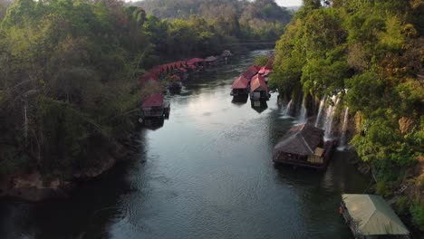 a stunning view of a river in thailand in the middle of the jungle, with waterfalls and a charming floating village on the side of the river - in sai yok national park in the province of kanchanaburi