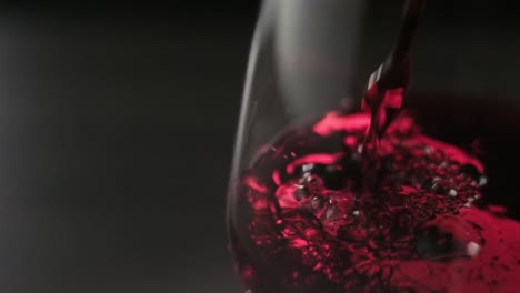 Slow-motion-shot-of-elegant-red-wine-pouring-and-splashing-into-Glass-wine,-Extreme-Close-up