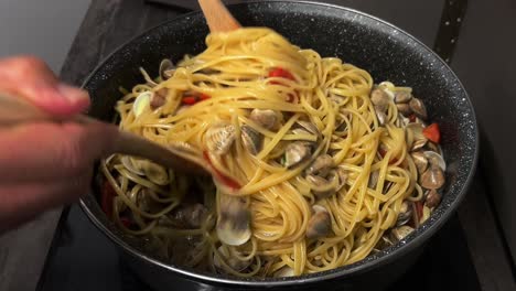 mezclando deliciosa pasta de linguina y almejas con tenedores de madera en sartén caliente