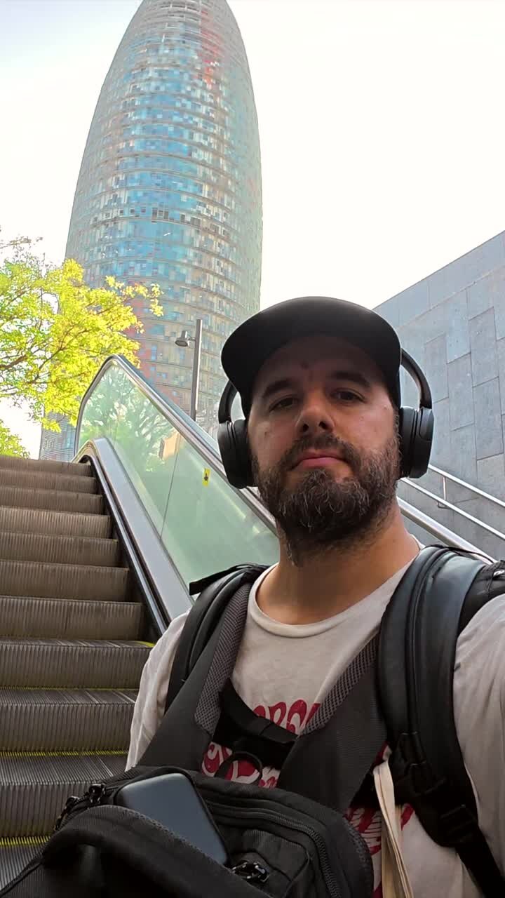 Man with headphones and backpack on an escalator near a modern building