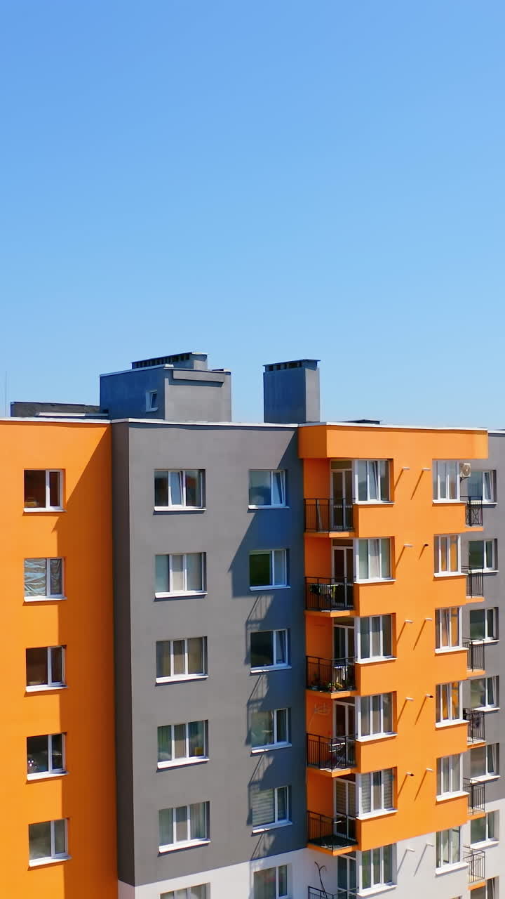 Bright multi-storey building in sunny day. Modern design of high-rise apartment building in the city. Exterior of new block of flats for residents under blue sky. Vertical video