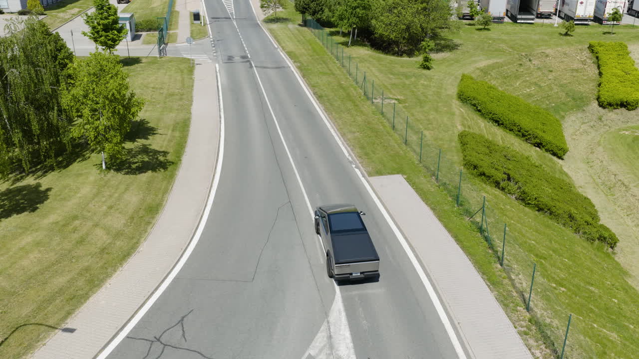 Aerial view following a modern EV car driving on a village road, sunny day