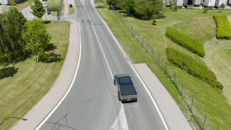 aerial view following a modern ev car driving on a village road, sunny day
