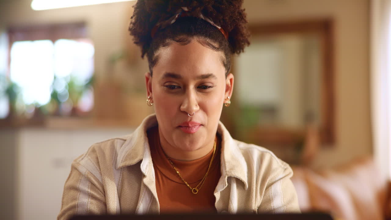 una mujer joven sonriendo mientras trabaja en su portátil en casa.