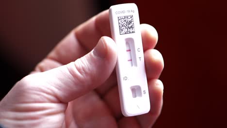 covid 19 positive antigen test with two red lines control and test in white caucasian male man hands and fingers as camera pans around slowly and he twists test slightly