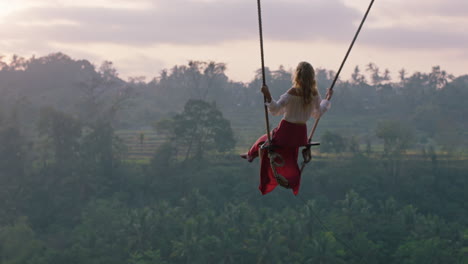 travel woman swinging over tropical rainforest at sunrise female tourist sitting on swing with scenic view enjoying freedom on vacation having fun holiday lifestyle slow motion