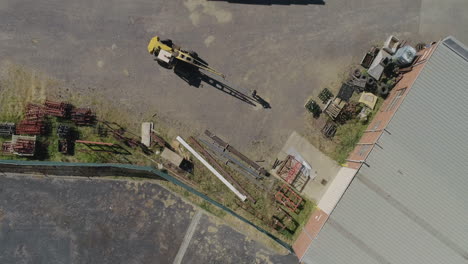 perspectiva aérea de una vieja grúa amarilla que mueve una barra de metal pesado con la ayuda de un trabajador de fábrica que mueve el producto específicamente a su lugar