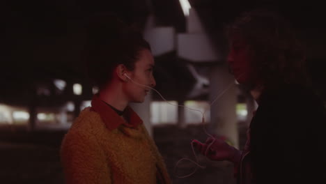 young couple sharing music under a city overpass at night