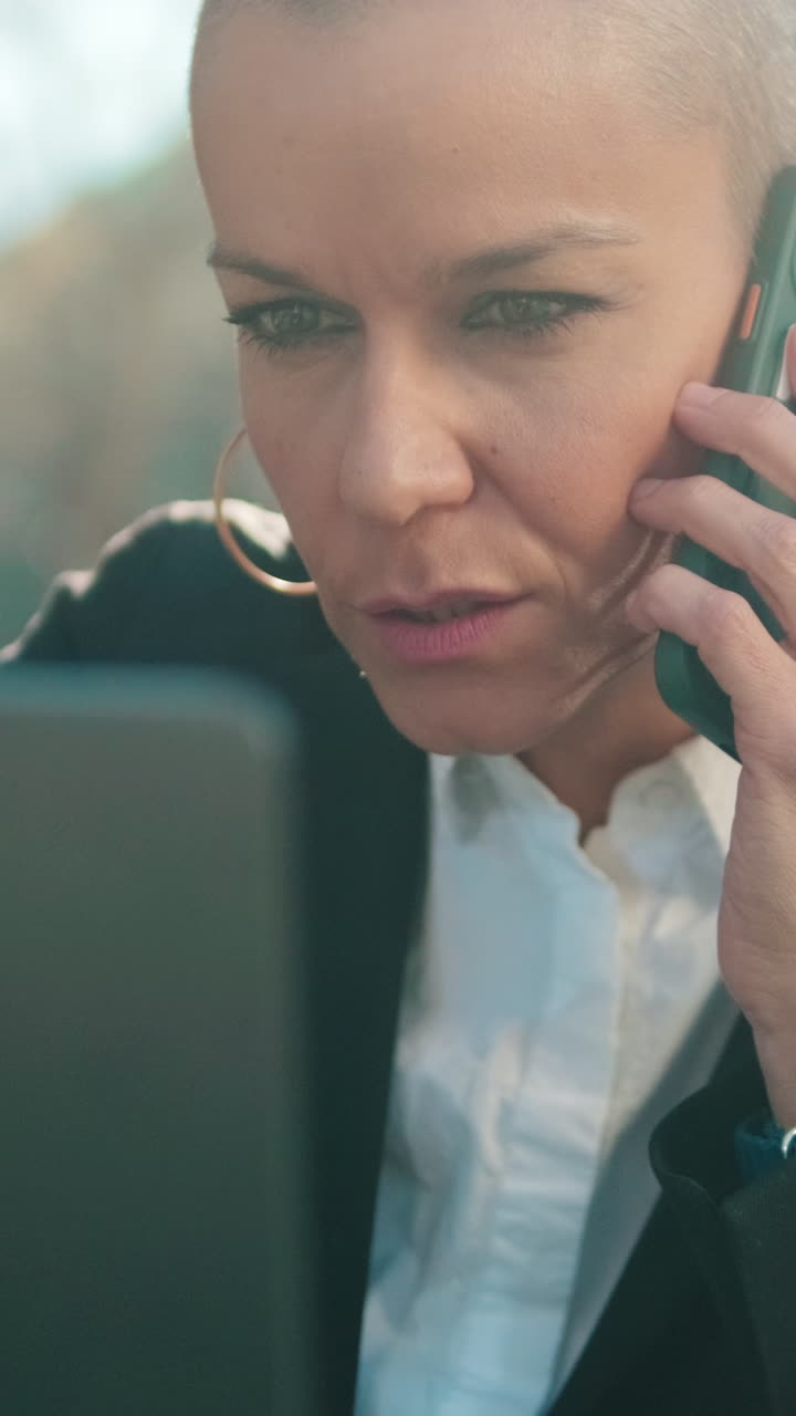 Focused Woman with Shaved Head Talking on Phone and Using Laptop
