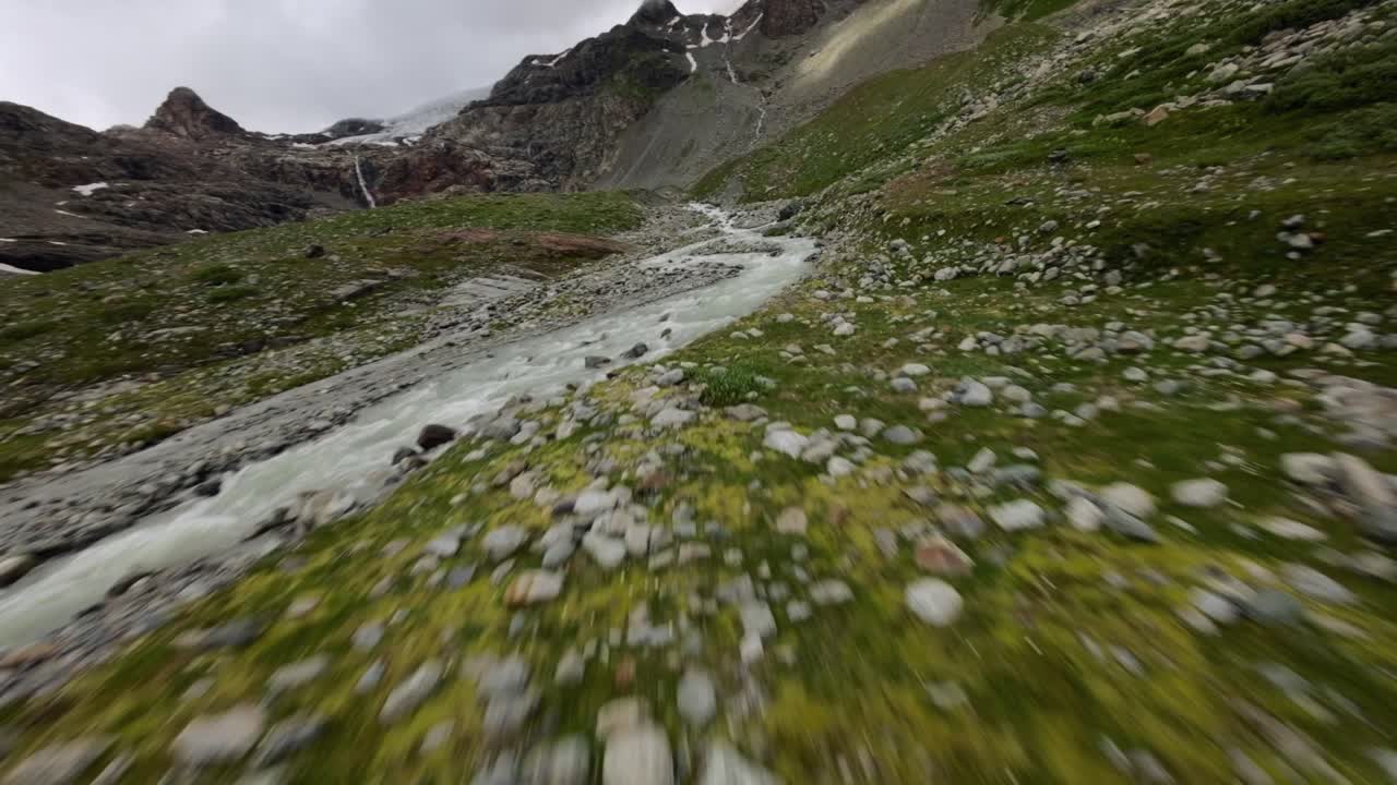 avión no tripulado de carreras fpv volando a alta velocidad sobre la corriente de agua que fluye en el glaciar fellaria en valmalenco de valtellina, italia