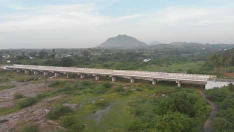 establishing cinematic aerial over a bridge in a green open field with a mountain in the background, car passing by, travel concept