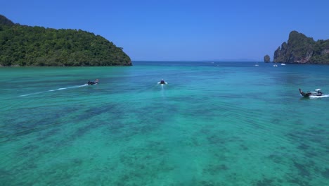 Koh-Phi-Phi-Bay,-colorful-traditional-longtail-boats-are-floating-on-calm-turquoise-water