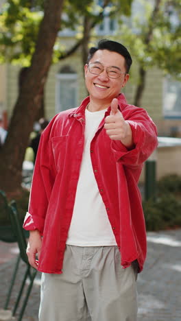 happy asian man showing thumbs up like sign positive something good positive feedback in city street