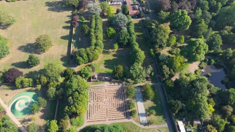 drone flyover starting at the maze and venusberg in cedar’s park, cheshunt, england, passing over buildings to the main road, with vibrant summer trees