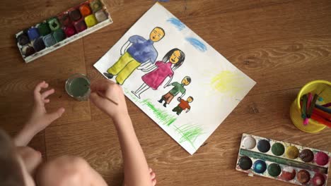 a child paints a drawing on the floor with watercolors. drawing depicting a family 05