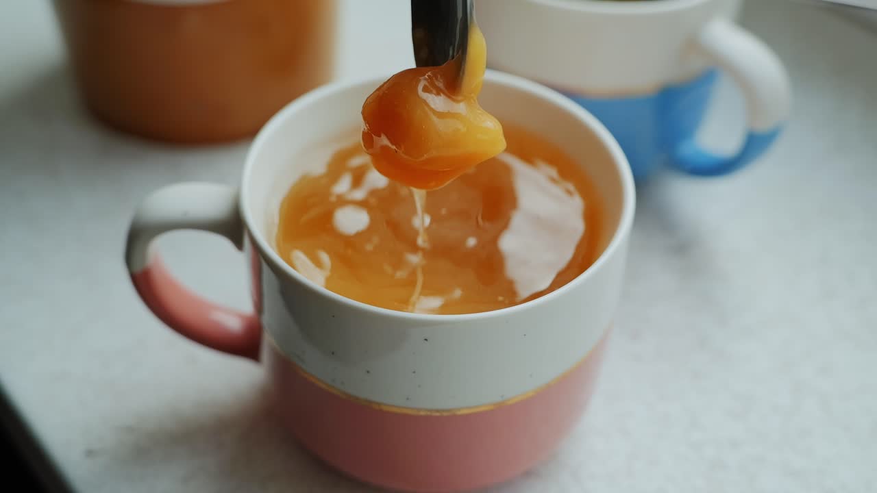 Close-up of golden honey melting in herbal tea inside cozy colorful ceramic mug
